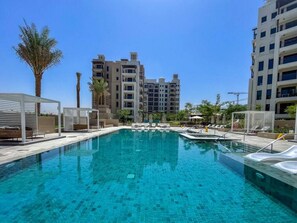 Una piscina con sillones de descanso y sombrillas, rodeada de edificios altos.