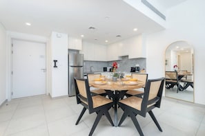 A modern kitchen with white cabinets, a stainless steel refrigerator, and a round dining table with four chairs.