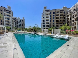 A swimming pool with lounge chairs, surrounded by multi-story buildings.
