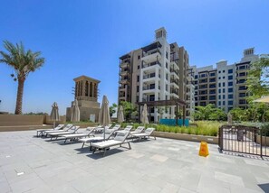 Zona de piscina en la azotea con tumbonas y sombrillas, rodeada de edificios altos.