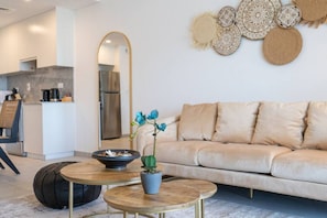En moderne stue med en beige sofa, et rundt træsofabord, en potteplante og dekorativ vægkunst.