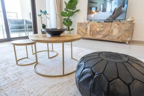 Una sala de estar moderna con una mesa redonda, dos taburetes a juego, un puf de cuero negro, un armario de madera y un televisor grande.