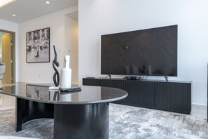 A modern living room with a round black table, a flat-screen TV mounted on the wall, and a minimalist decor.