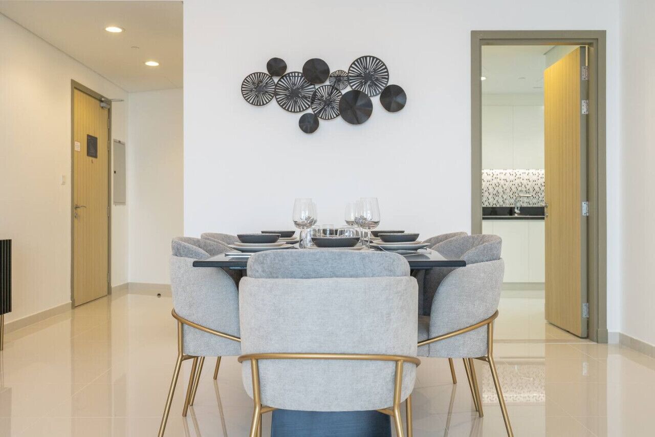 Een eethoek met een tafel voor vier personen, grijs gestoffeerde stoelen en een decoratief object aan de wand.