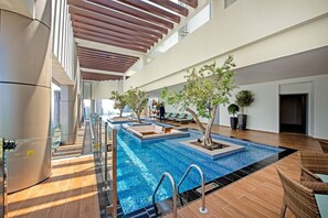 Una piscina interior moderna con agua cristalina, rodeada de zonas de descanso y plantas en macetas.