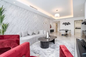 A modern living room with a marble wall, a grey sofa, red chairs, a coffee table, and a dining area with a table and chairs.