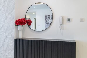 Ein modernes Badezimmer mit einem runden Spiegel, einer weißen Vase mit roten Blumen, einem weißen Telefon und einem Thermostat an der Wand.