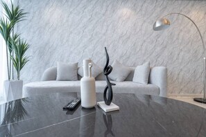 Ein modernes Wohnzimmer mit Marmorwand, einem weißen Sofa, einem schwarzen Couchtisch, einer Stehlampe und einem Blumentopf.