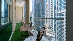 Un balcon donnant sur des immeubles de grande hauteur, une petite table, une chaise et une plante en pot.