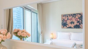 Une chambre d’hôtel avec un lit, une table de chevet, une lampe, un vase de fleurs et une grande fenêtre avec des rideaux.