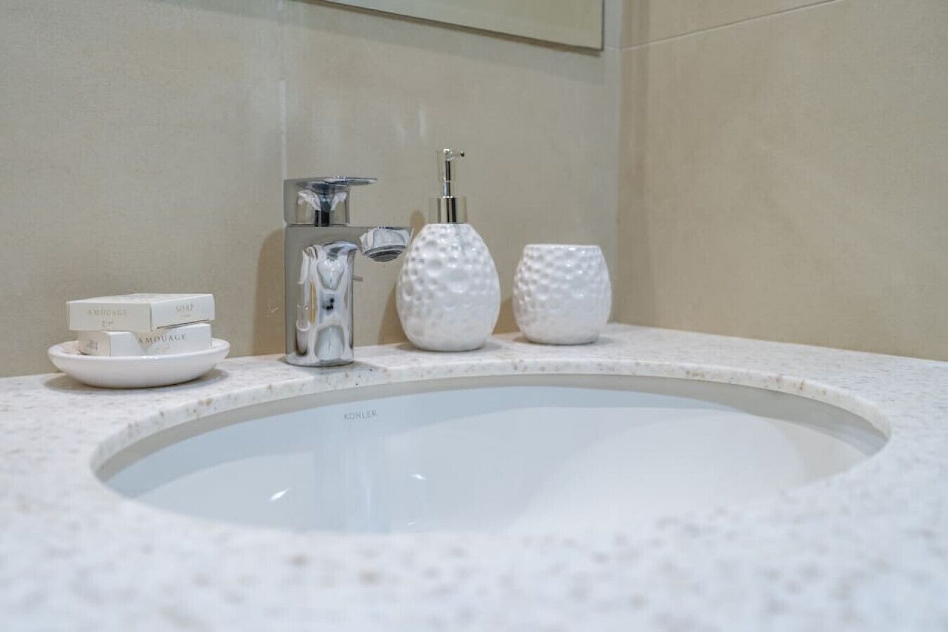 Un lavamanos de baño con grifo Kohler, jabón y dos saleros y pimenteros con textura sobre la encimera.