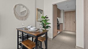 Un comedor con una mesa de madera dispuesta para dos personas, un espejo redondo y una obra de arte enmarcada en la pared.