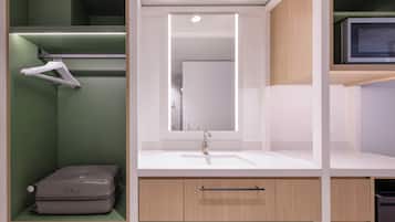 Un baño moderno con un lavabo blanco, un espejo y una maleta sobre una estantería.