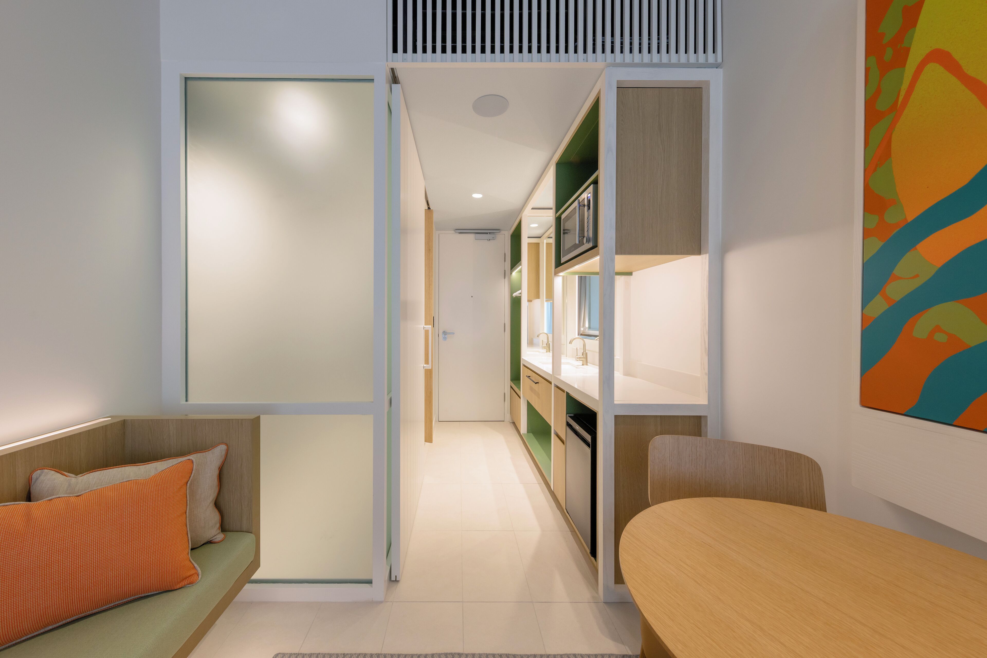 A modern kitchen with a central island, a dining area with a wooden table, and a sofa with orange cushions.