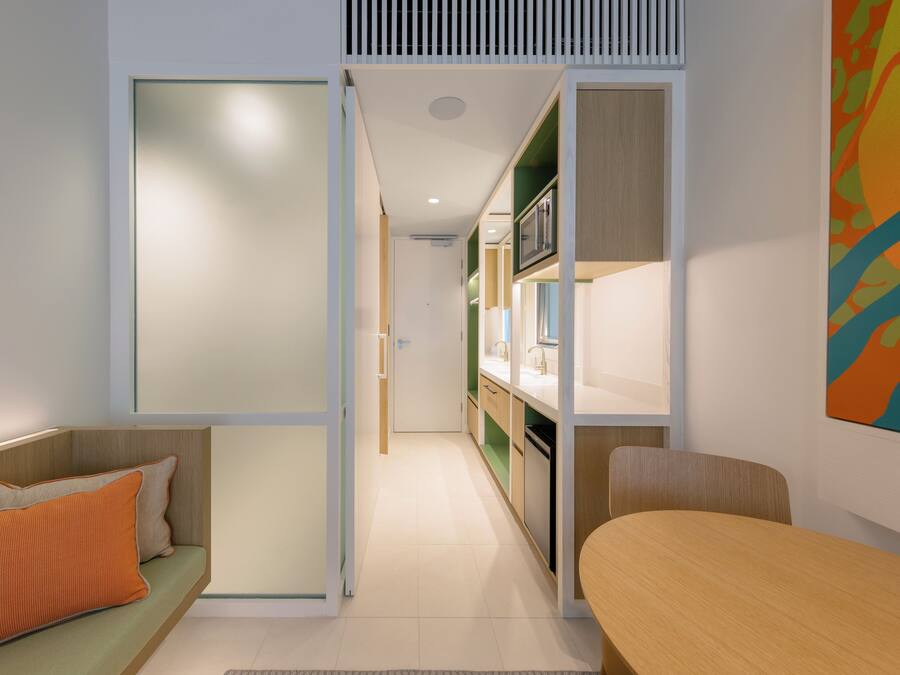 A modern kitchen with a central island, a dining area with a wooden table, and a sofa with orange cushions.