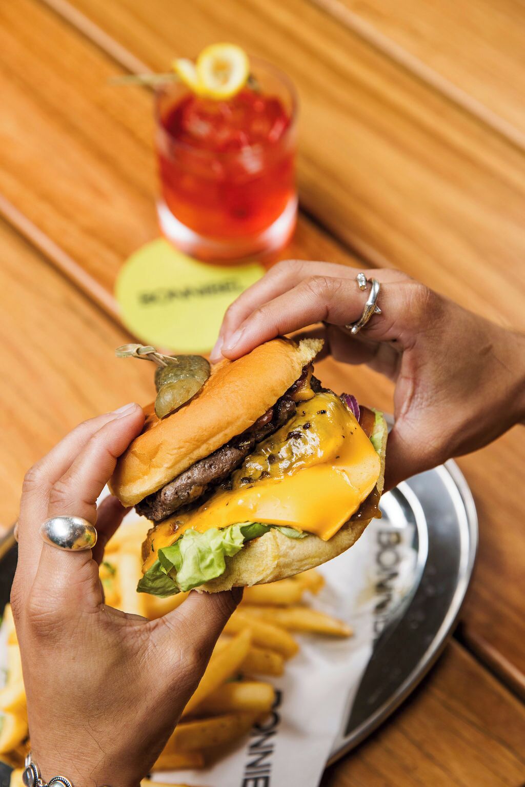 A person holding a burger with a bun, cheese, lettuce, and a beef patty.
