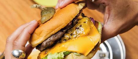 A person holding a burger with a bun, cheese, lettuce, and a beef patty.