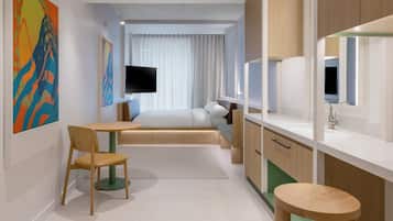 A modern hotel room with a bed, a TV, a desk, and a chair.