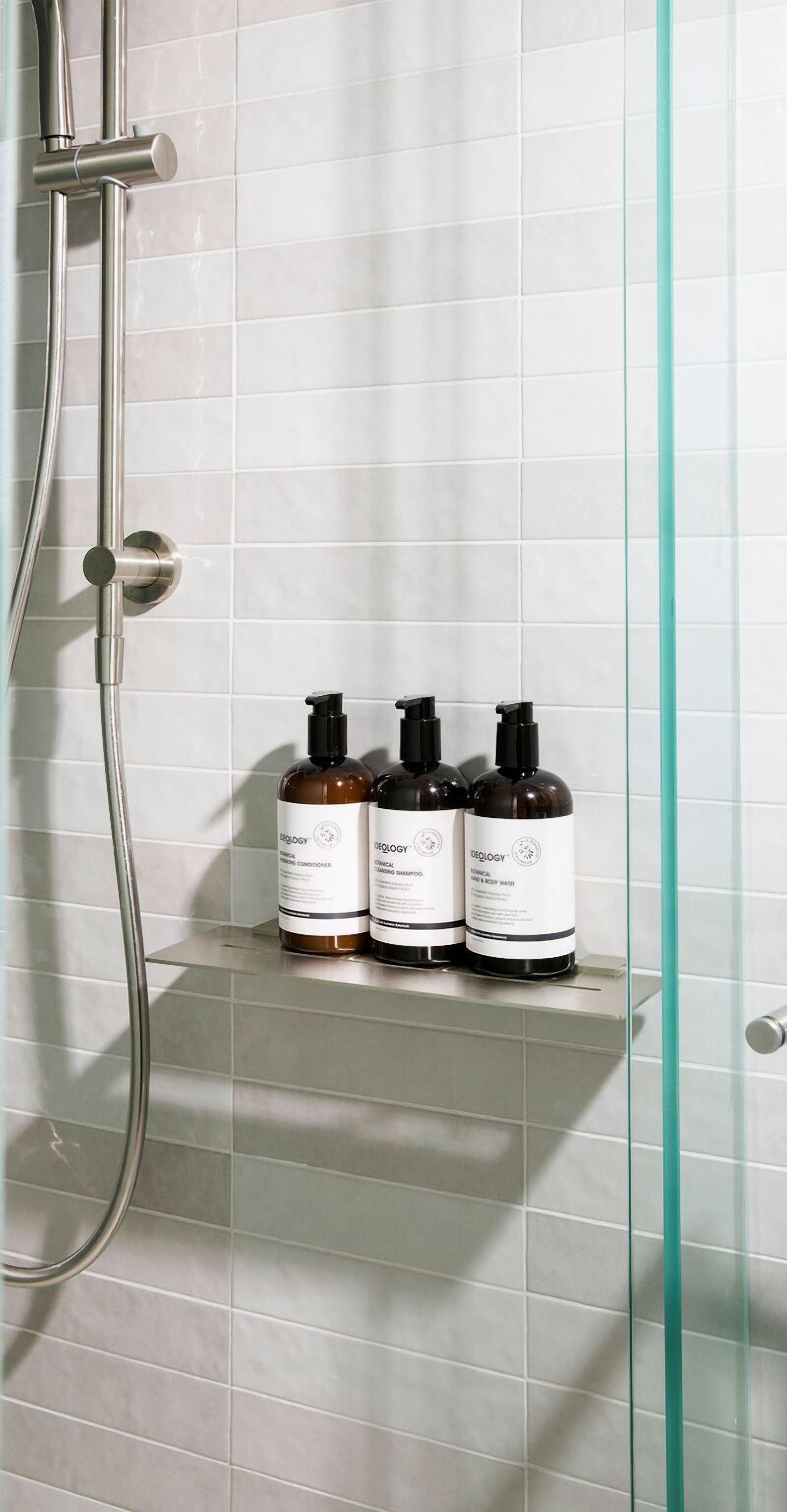 A bathroom with a glass shower enclosure, a chrome showerhead, and three bottles of toiletries on a shelf.