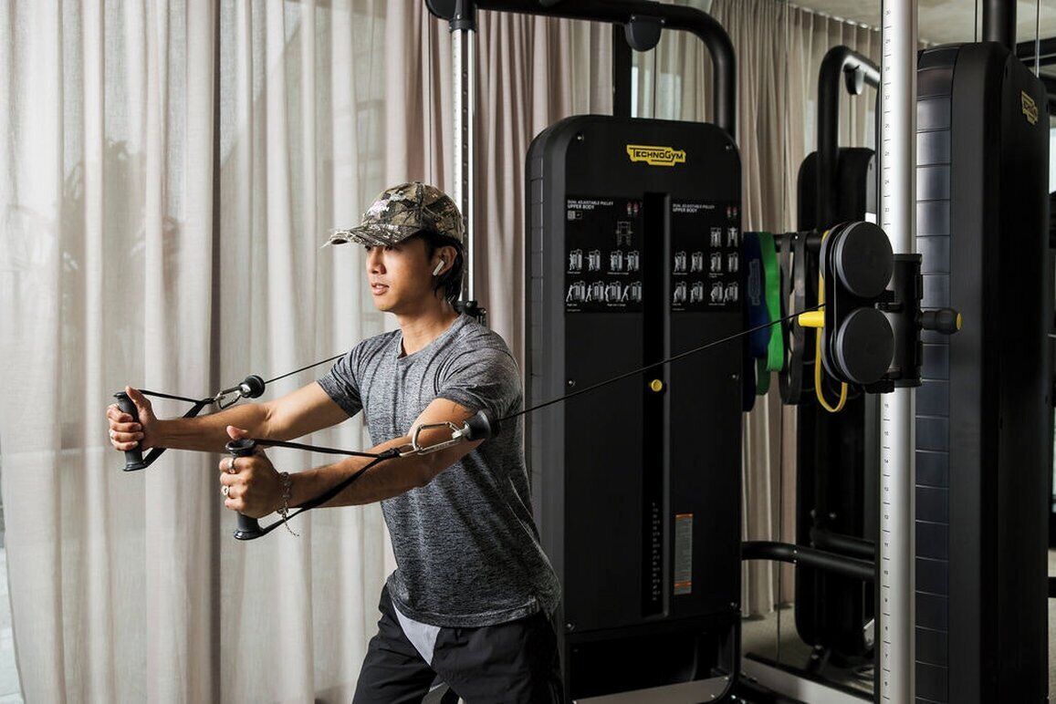 A person using resistance bands in a gym with exercise machines and a mirror.