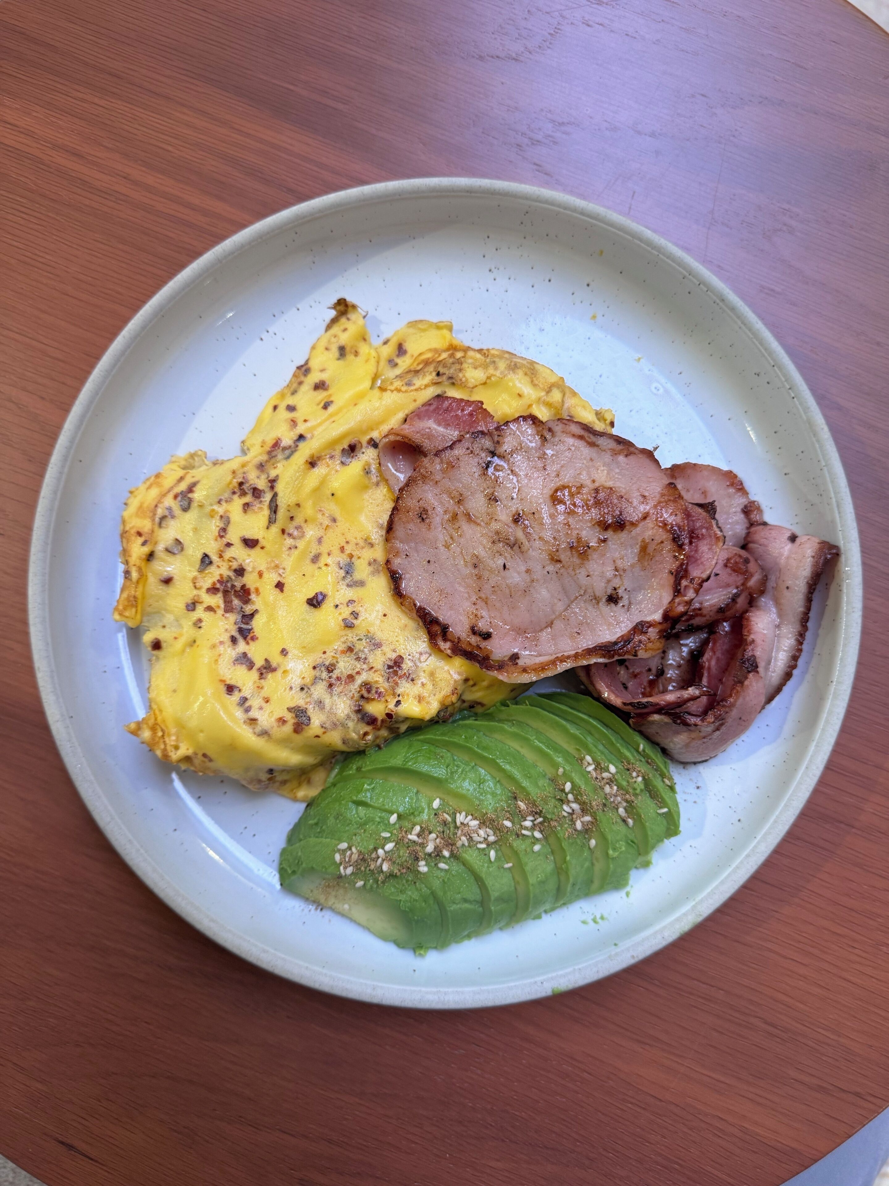 A plate with an omelette, ham, and avocado on a ceramic plate.