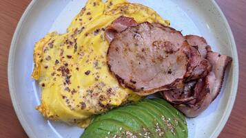 Une assiette en céramique contenant une omelette, du jambon et un avocat.