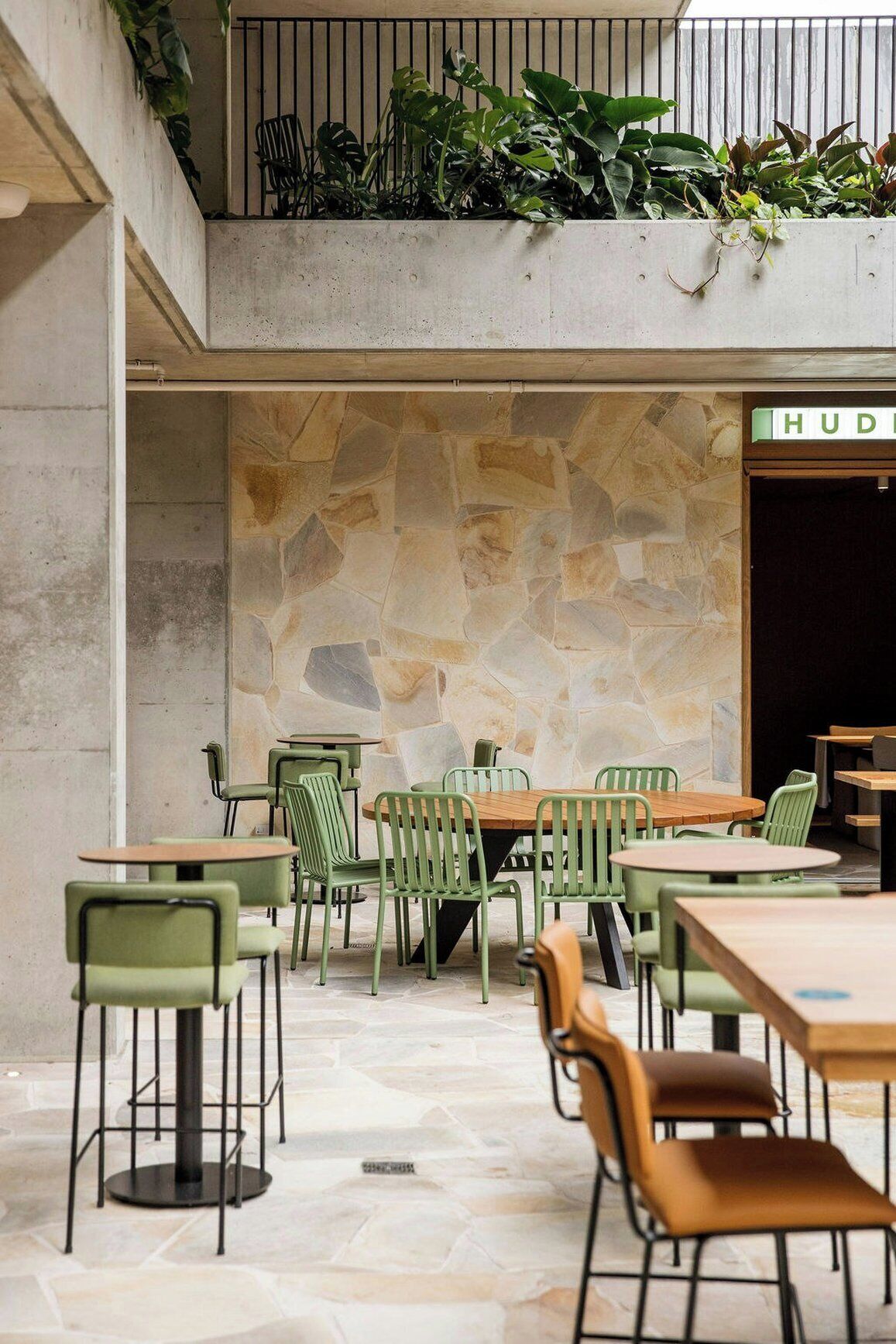 A café with green chairs and tables, a stone wall, and a sign that reads 'HUD'.