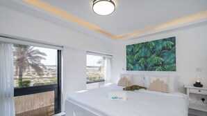 Une chambre d’hôtel avec un grand lit, une vue sur les palmiers et un tableau représentant des feuilles tropicales accroché au mur.