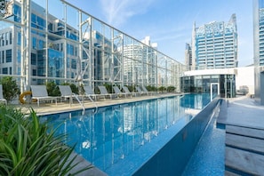 A rooftop pool with lounge chairs, glass railings, and modern buildings in the background. - The Pad 1109 - Business Bay · Cosmopolitan Apartment with Burj Khalifa View (Dubai)