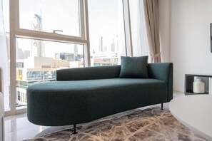 Un salon moderne avec un canapé vert foncé, un tapis à motifs et une vue sur le paysage urbain, visible à travers de grandes fenêtres.