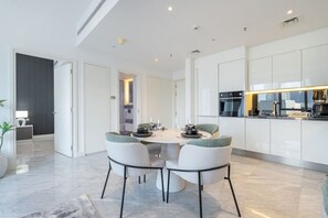 A modern kitchen with white cabinets, a dining area with a round table and chairs, and a visible oven and microwave. - The Pad 1109 - Business Bay · Cosmopolitan Apartment with Burj Khalifa View (Dubai)