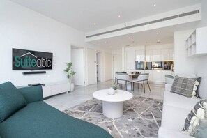 Una sala de estar moderna con un sofá, una mesa de centro y un comedor con sillas. Se ve una cocina al fondo.