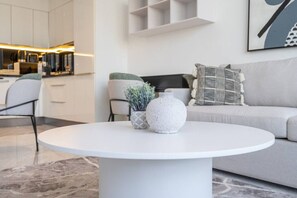 A modern living room with a round white coffee table, a grey sofa, and a kitchen area in the background. - The Pad 1109 - Business Bay · Cosmopolitan Apartment with Burj Khalifa View (Dubai)