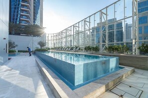 Ein moderner Außenpool mit Glasverkleidung, umgeben von einem Hochhaus und einer Person, die das Pool-Areal reinigt.