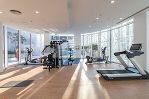 A modern gym with cardio machines, weightlifting equipment, and large windows offering views of the outdoors. - The Pad 1109 - Business Bay · Cosmopolitan Apartment with Burj Khalifa View (Dubai)