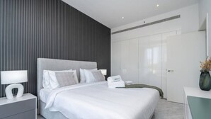 A modern bedroom with a large bed, a bedside table with a lamp, and a wardrobe.