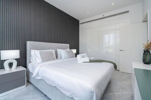 Un dormitorio moderno con una cama grande, una mesita de noche con lámpara y un armario.