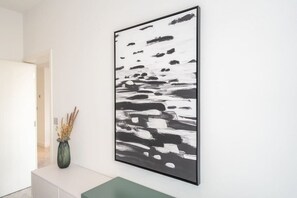 Un intérieur moderne agrémenté d’un grand tableau abstrait au mur, d’une console au design minimaliste et d’un vase contenant des plantes séchées.