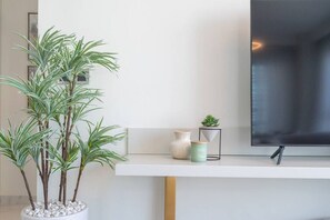A modern living room with a white console table, a large potted plant, a small succulent, and a flat-screen TV on a stand.