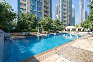 Una piscina con sillas de descanso, rodeada de árboles y edificios altos.