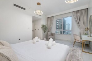 A modern hotel room with a large bed, a desk, and a view of the city through the window.