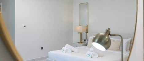 Habitació d'hotel amb un llit, una làmpada de nit, un mirall i una taula petita amb una làmpada.