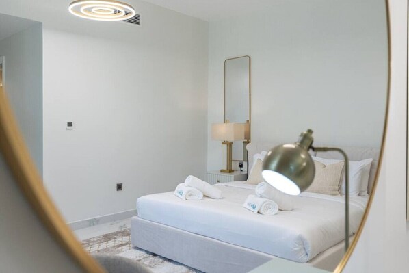 A hotel room with a bed, a bedside lamp, a mirror, and a small table with a lamp.
