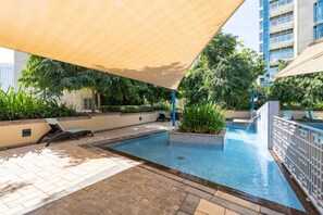 A swimming pool with a sunshade, lounge chairs, and greenery.