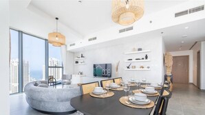 A modern dining area with a round table set for six, a grey sofa, and a television on the wall.