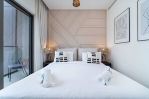 Une chambre d’hôtel avec un grand lit, deux tables de chevet avec des lampes, une chaise et une vue sur l’extérieur, visible à travers une porte vitrée.