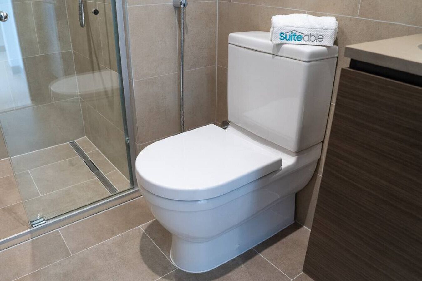 A modern bathroom with a white toilet, a glass shower enclosure, and a visible 'suiteable' towel.