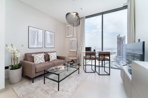 Un salon moderne avec un canapé, une table basse et des fauteuils, une grande fenêtre donnant sur la ville et des œuvres d’art accrochées au mur.