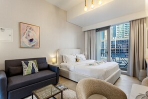 Une chambre d’hôtel moderne, équipée d’un lit, d’un canapé, d’une table basse et offrant une vue sur la ville grâce à de grandes fenêtres.