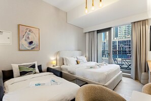 A hotel room with two beds, a large window with a city view, a painting on the wall, and a balcony with chairs.
